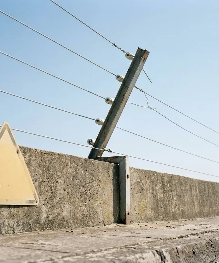 Haste de cerca elétrica em L inclinada para dentro do terreno, com placa de advertência